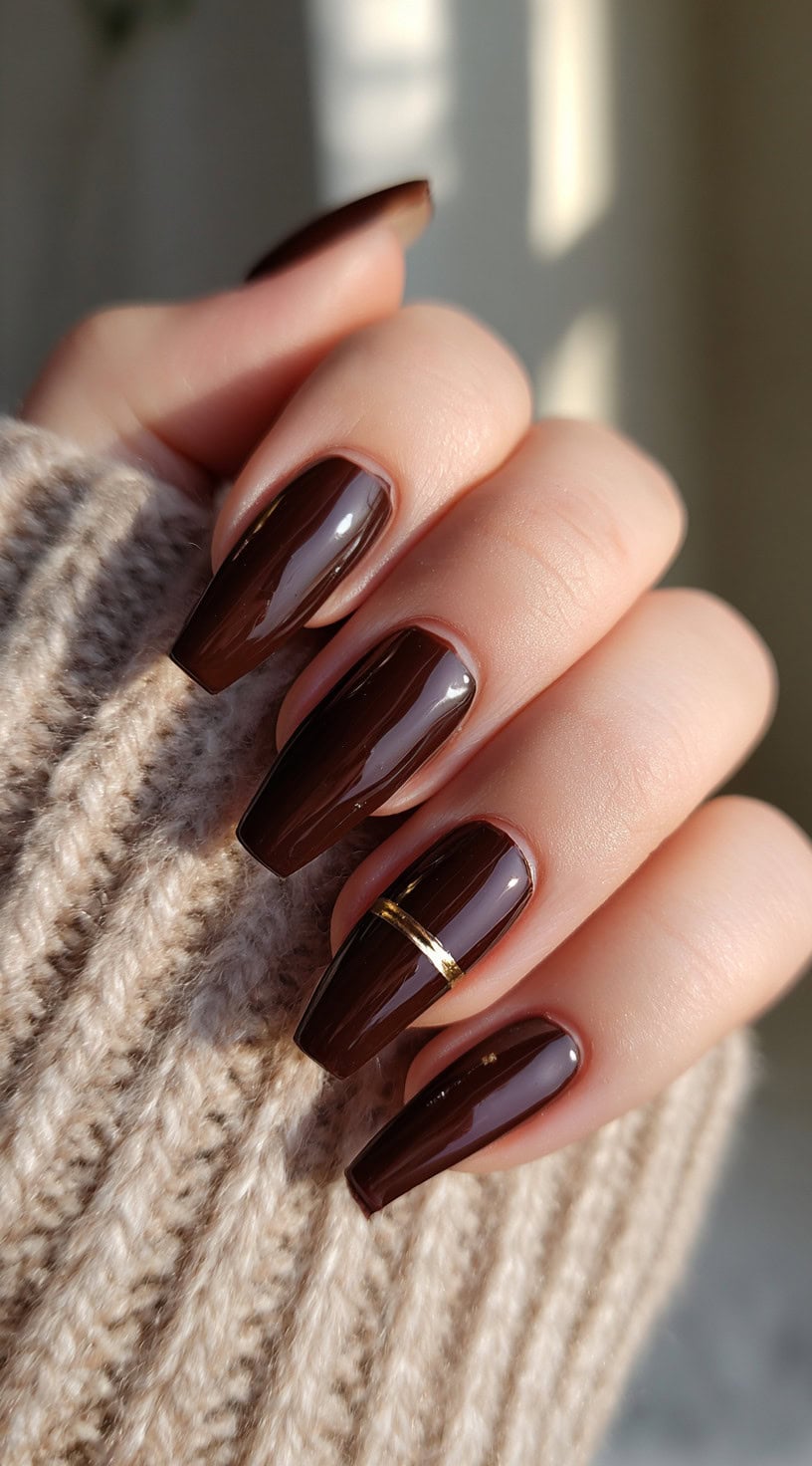 Coffin-shaped chocolate brown nails with one accent nail featuring a single horizontal gold band.