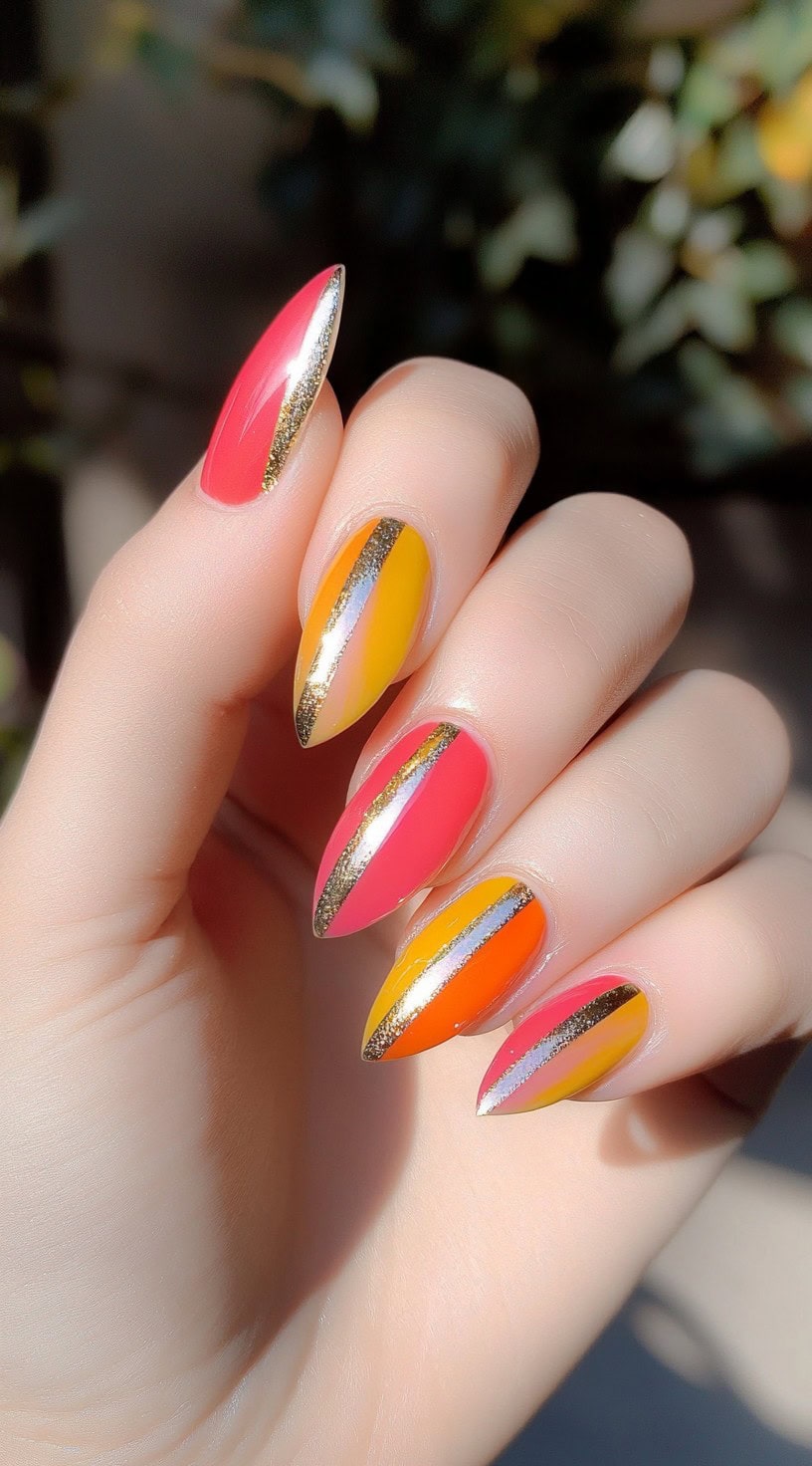 Almond-shaped nails with pink, yellow, and orange color-blocked panels divided by gold glitter stripes.