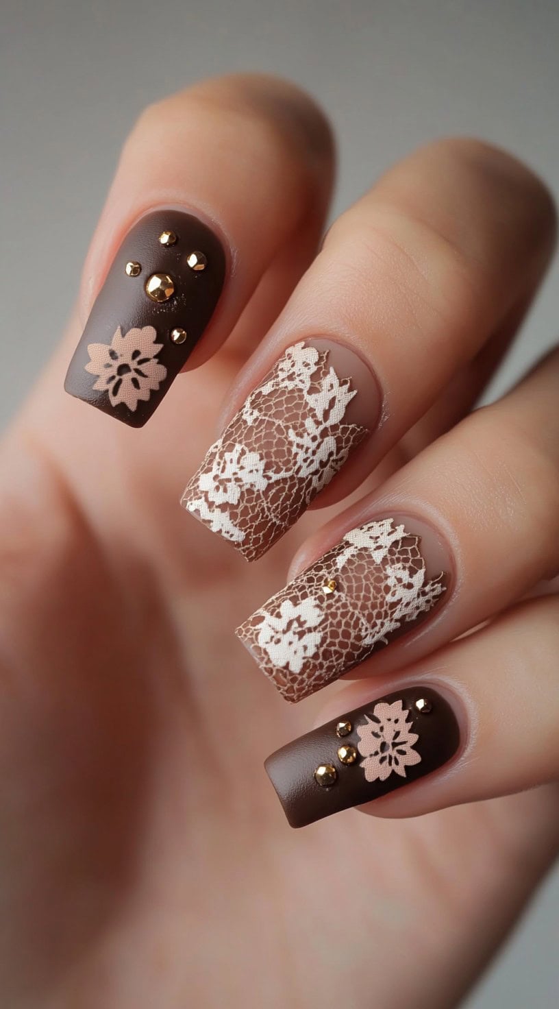 Square-shaped nails painted in deep brown, featuring matte floral lace patterns, gold studs, and glossy accents.