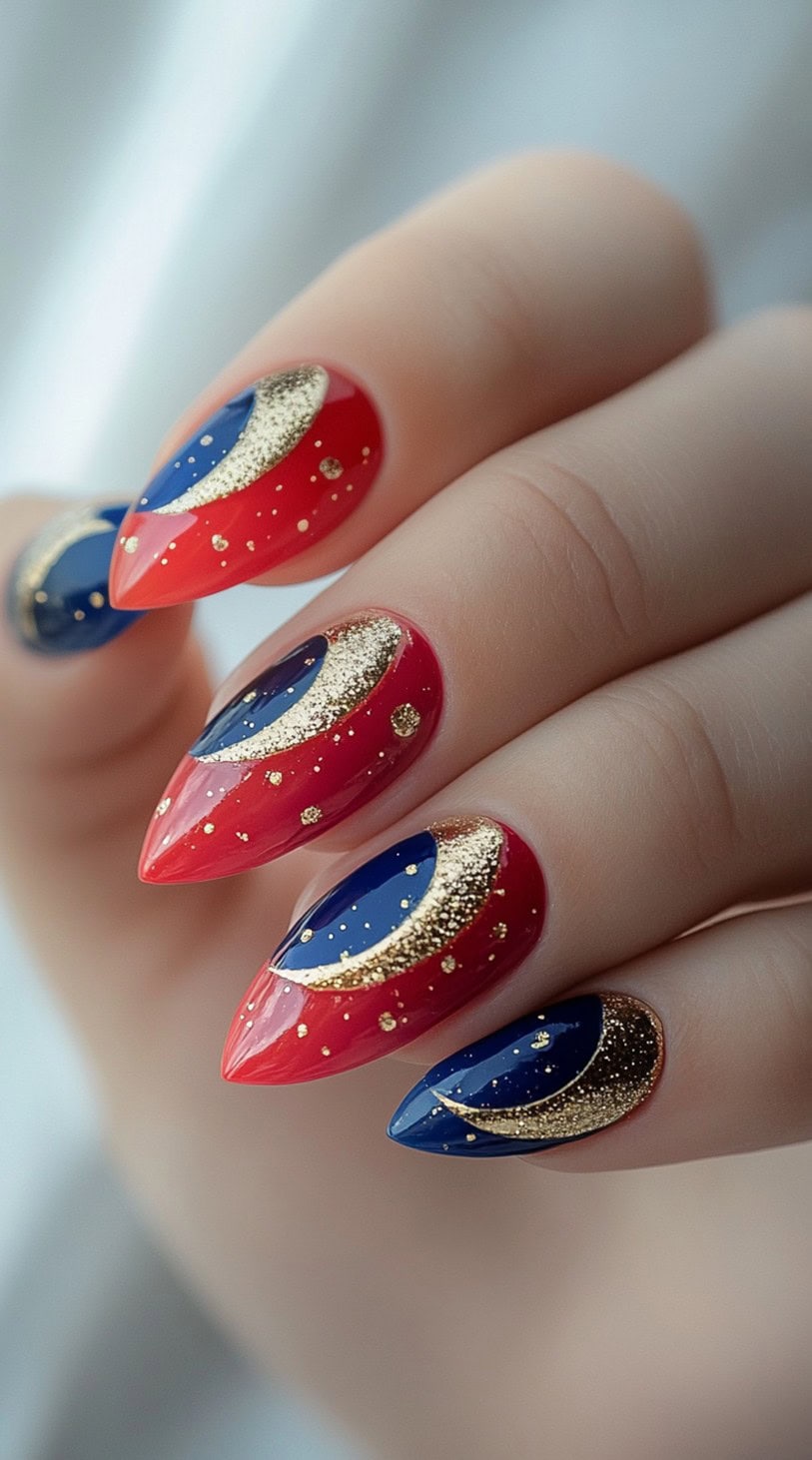 A hand with stiletto-shaped nails featuring bold red and blue crescent moon designs, accented with shimmering gold glitter.
