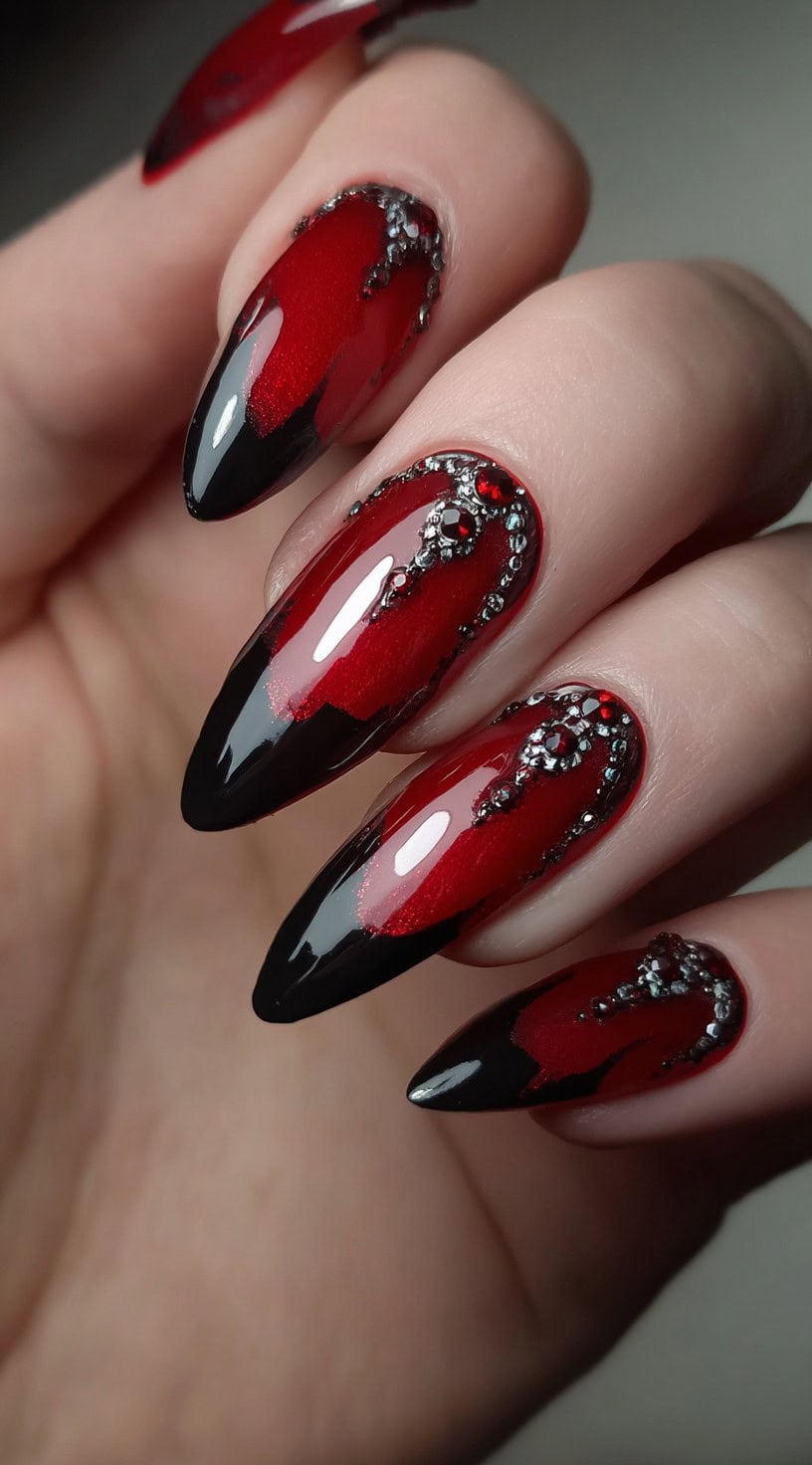 Almond-shaped nails in shimmering crimson with glossy black tips and encrusted red gemstones.