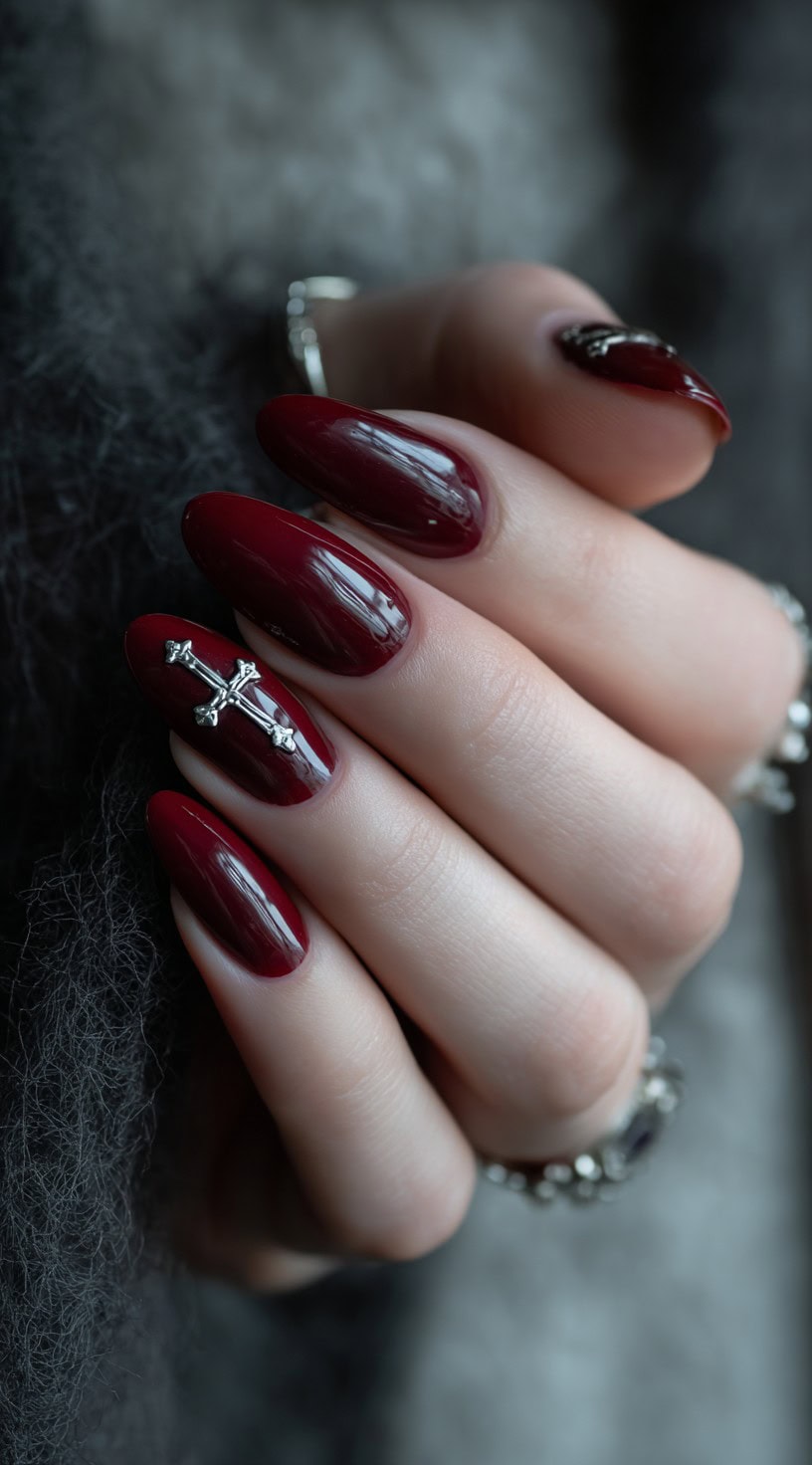 Oval-shaped nails painted a rich, glossy crimson with 3D silver cross embellishments.