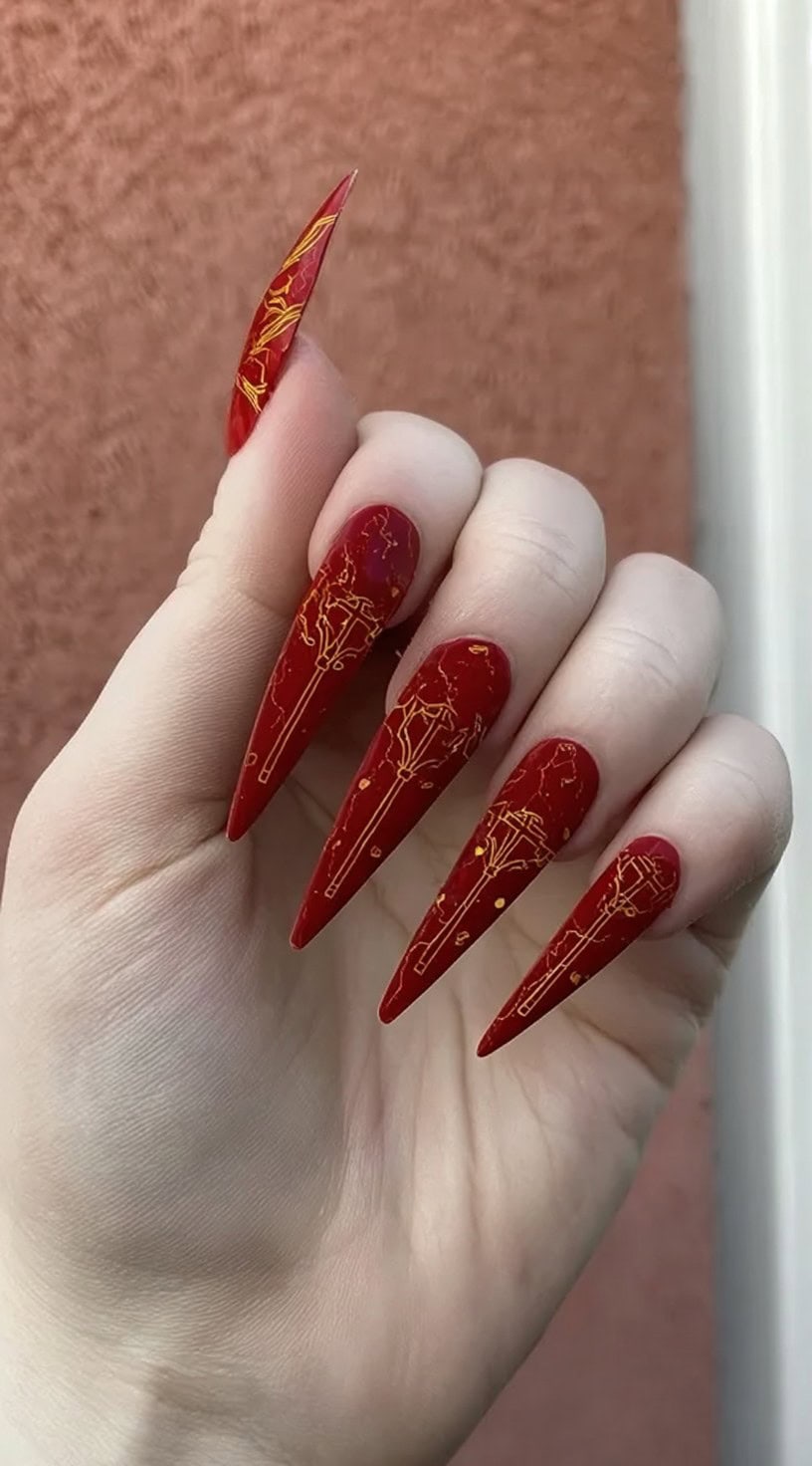 Ultra-long dagger-shaped nails in rich crimson with fine gold linework resembling arcane symbols.
