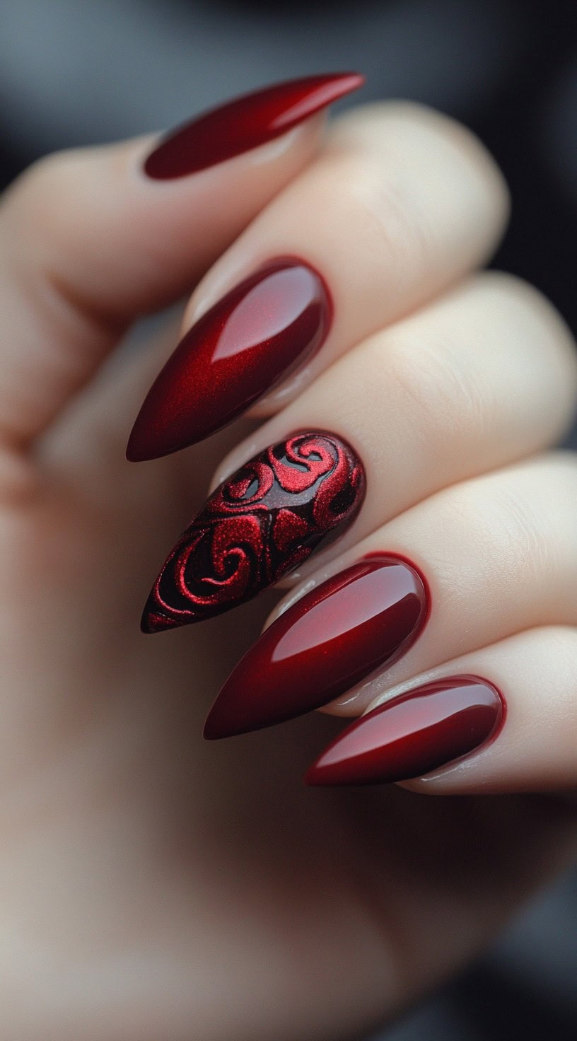 Crimson stiletto nails featuring glossy polish with a textured velvet rose pattern on one accent nail.