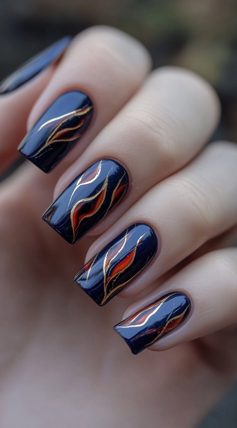 A hand showcasing square-shaped nails painted in deep navy blue, with intricate red and gold flame designs flowing across each nail.