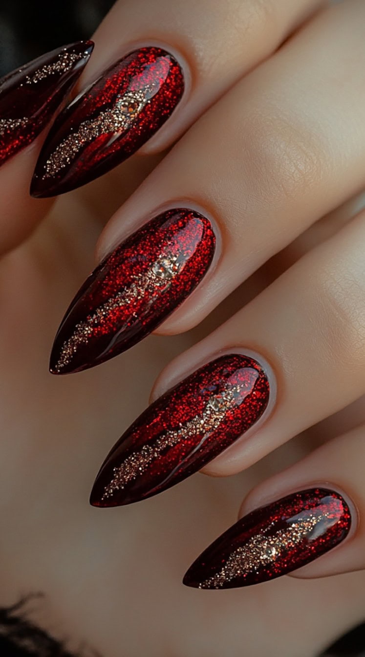 A set of almond-shaped nails with a deep red base covered in shimmering glitter, featuring streaks of gold foil for an elegant and dramatic effect.