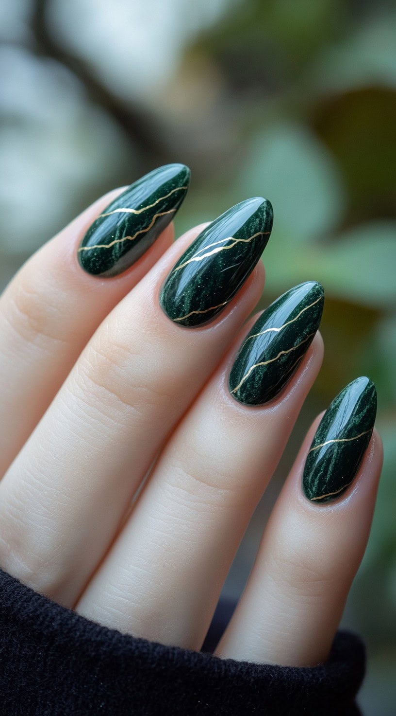 A set of almond-shaped nails in a deep, glossy green, featuring a marbled effect with fine gold veining details.