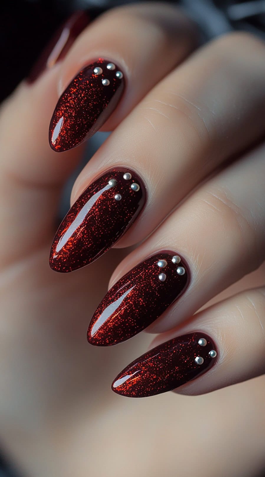 A deep red glitter manicure with a glossy finish, adorned with small pearl accents on an almond-shaped nail.