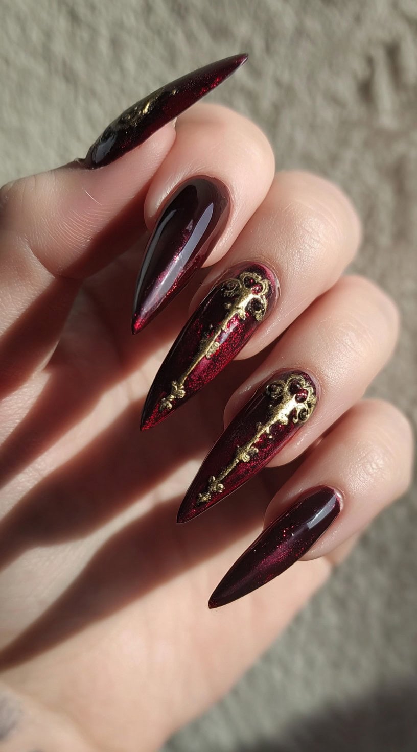 Long stiletto nails painted a shimmering blood-red with regal gold embellishments resembling royal insignias.