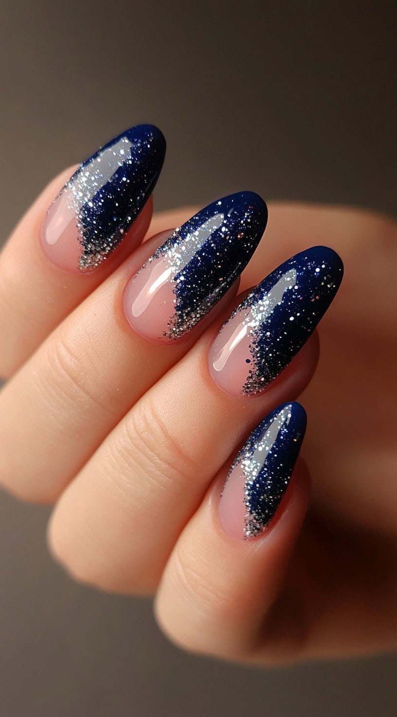 Almond-shaped nails featuring a deep navy base with a silver glitter gradient from the cuticles.