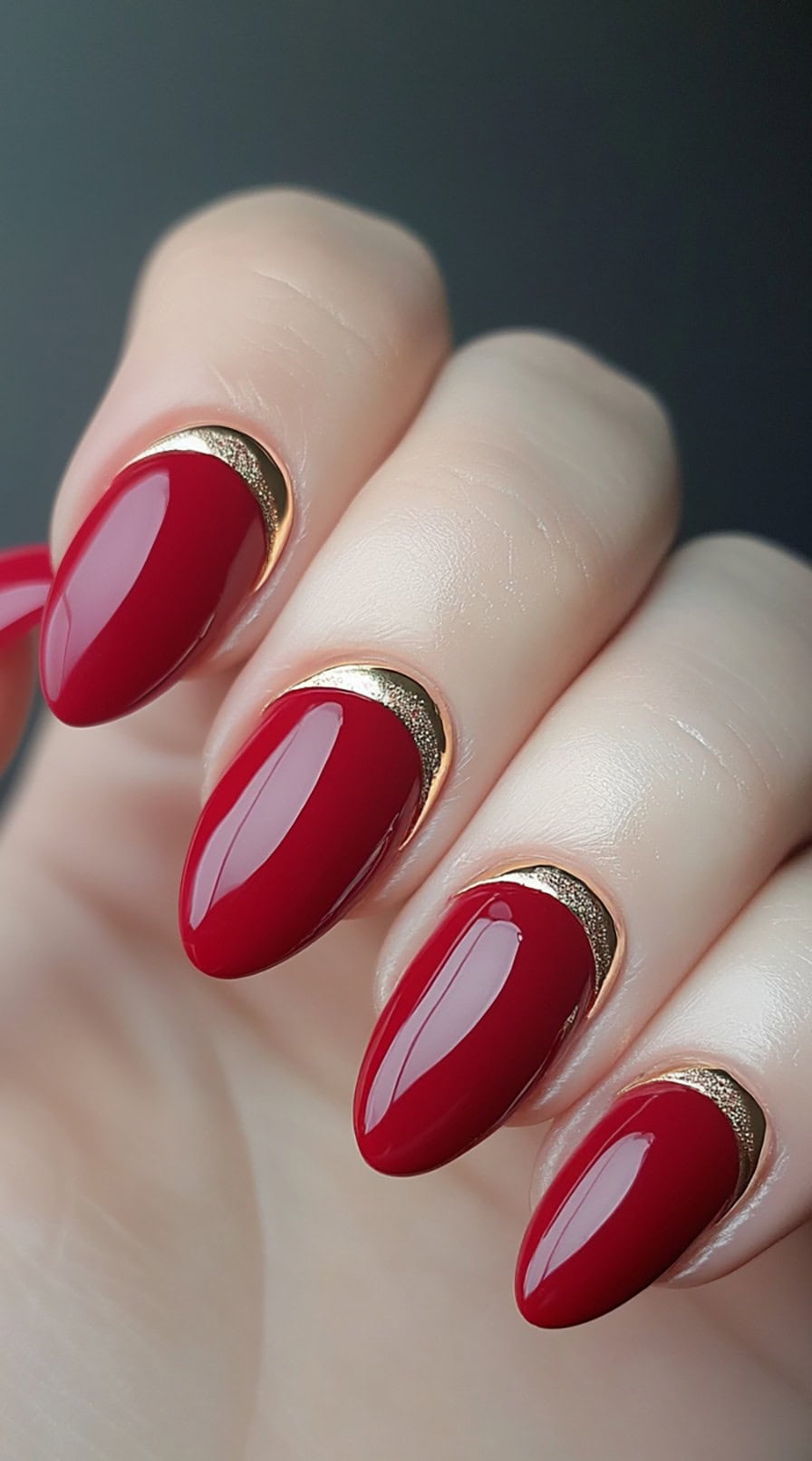 Glossy deep red oval nails with metallic gold half-moon details outlining the cuticles.