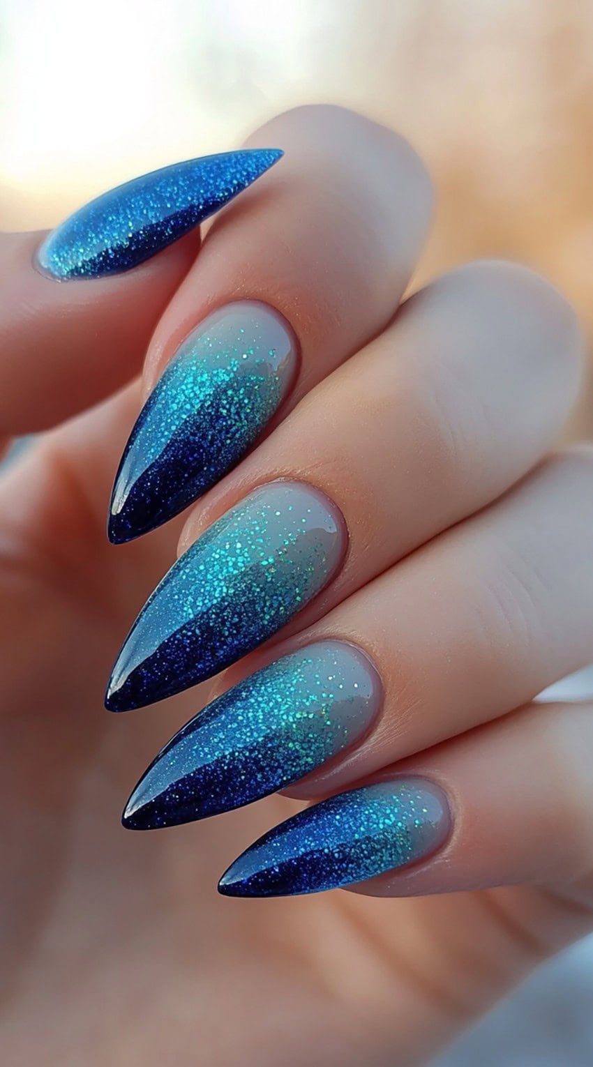 Stiletto nails with a sapphire to soft gray ombre and aqua blue glitter gradient.