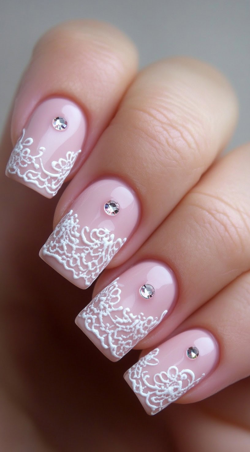 Soft pink nails with intricate white lace-like French tips and subtle rhinestone accents.