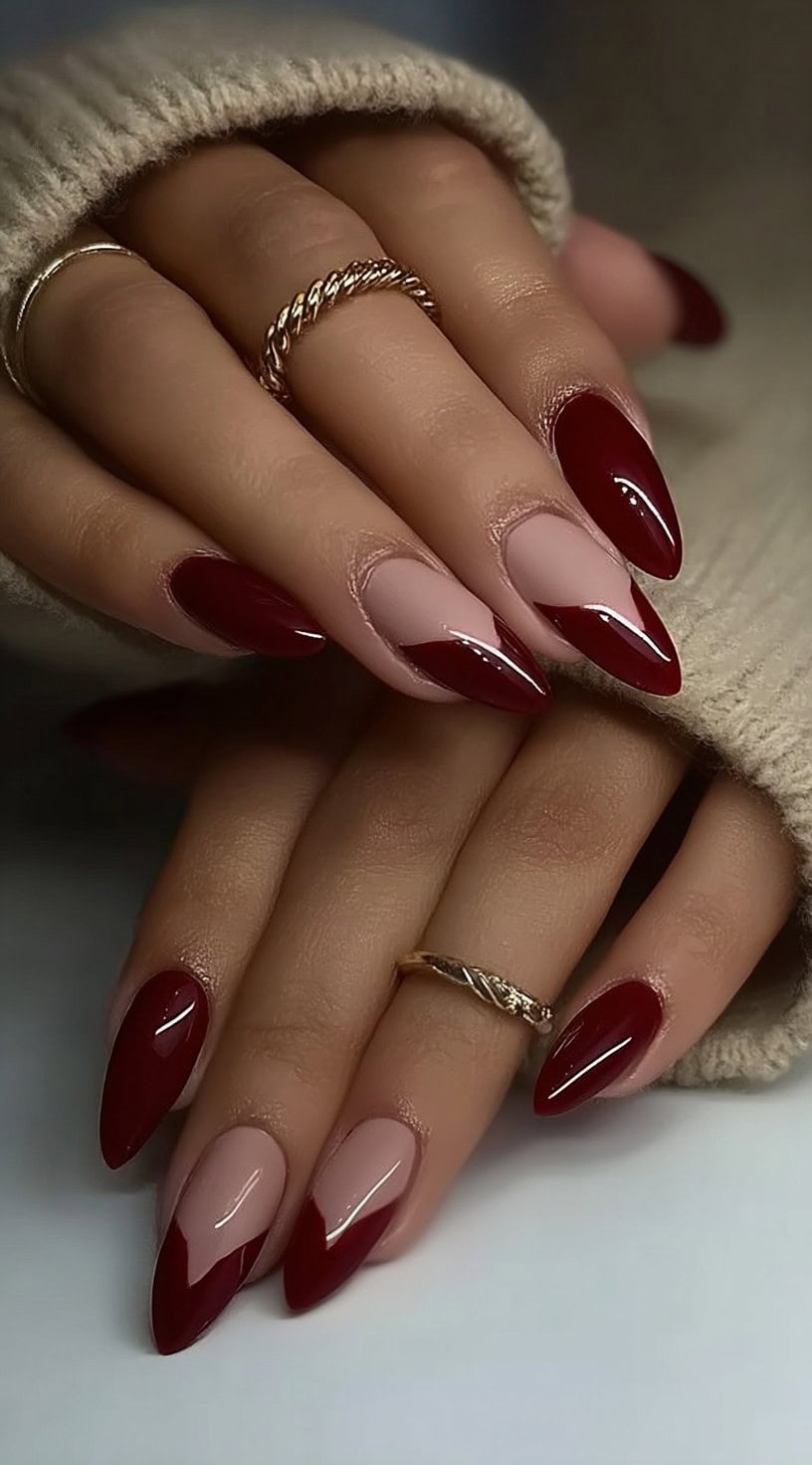 A pair of hands showing almond-shaped nails with diagonal burgundy tips over a glossy nude base.