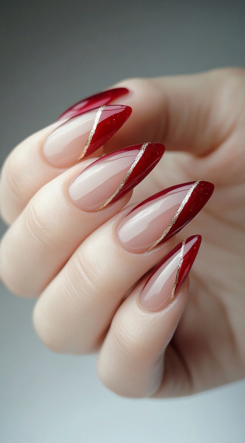 A set of almond-shaped nails featuring a diagonal red French tip design, accentuated with fine gold glitter lines for a modern touch.