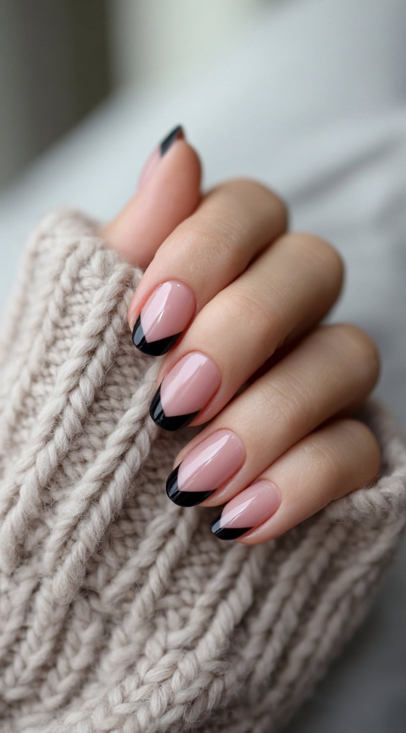 A hand with almond-shaped nude nails featuring diagonal black French tips.