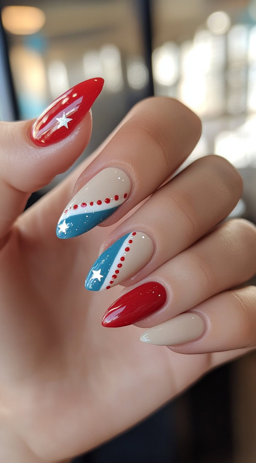 A hand with almond-shaped nails featuring a mix of red, white, and blue diagonal stripes, star embellishments, and dotted details.