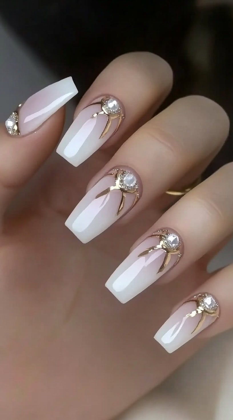 A sophisticated French tip manicure featuring white tips and gold embellishments with rhinestone accents for a glamorous touch.