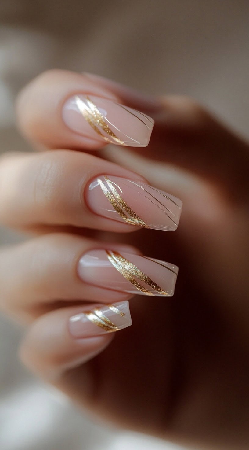 A close-up of square-shaped nails with a nude base and delicate gold swirls accented by thin black lines.