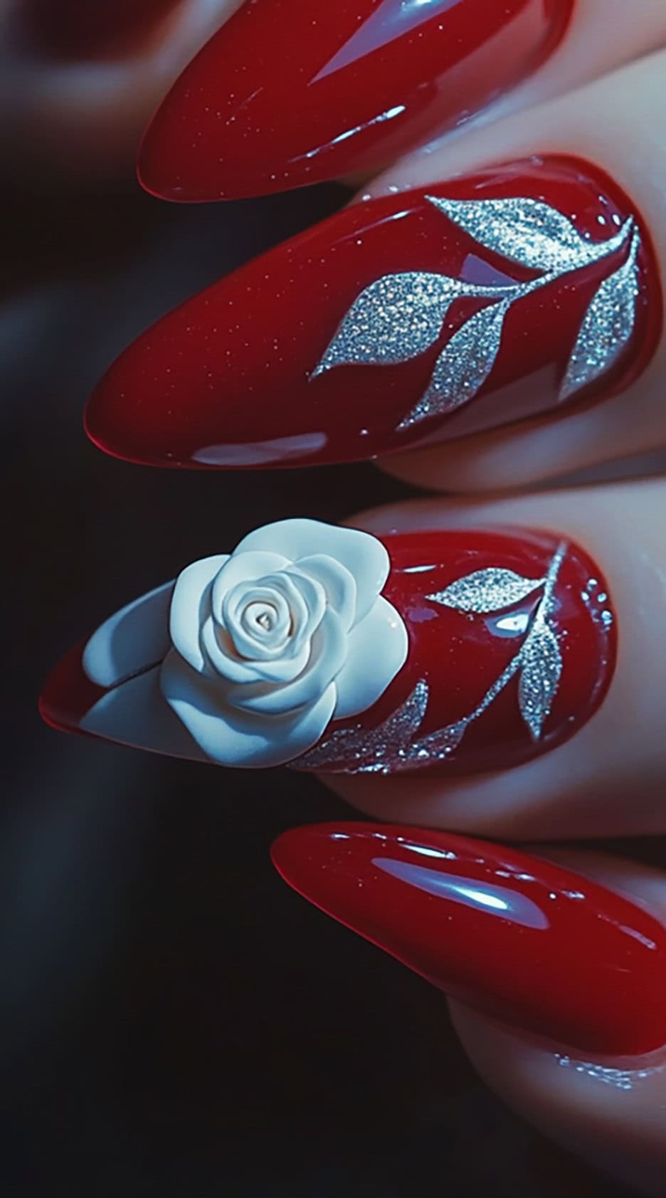 Glossy red almond-shaped nails featuring a stunning 3D white rose and delicate silver leaf designs.