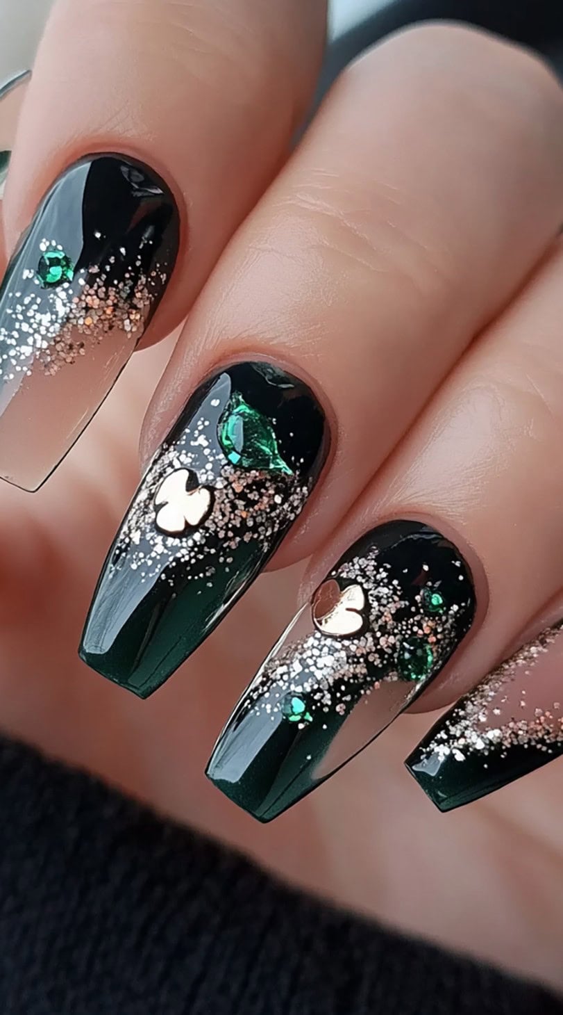 Long coffin-shaped nails with black-to-emerald ombre, gold glitter, and shamrock charms.