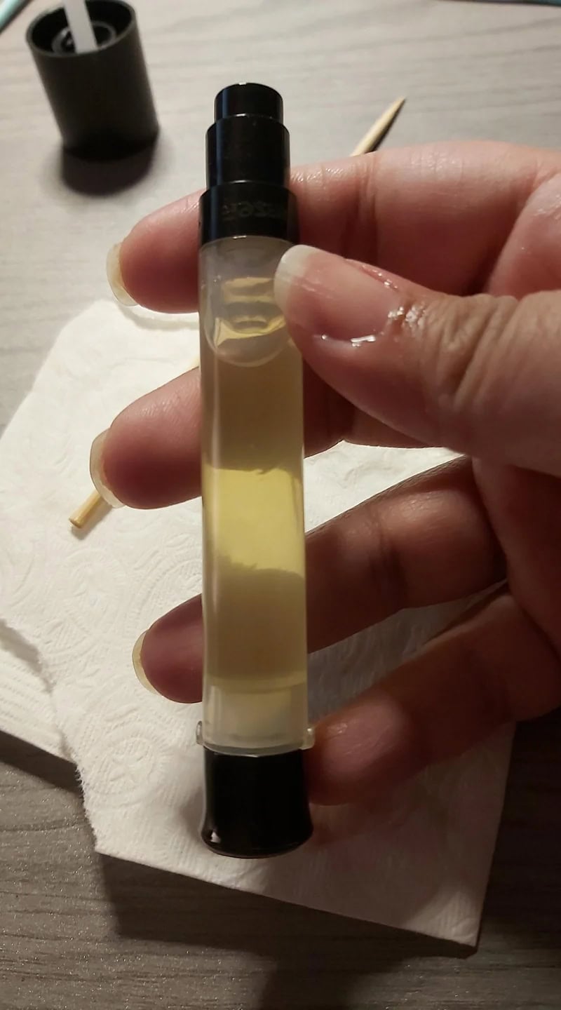A freshly filled clear tube of DIY cuticle oil held above a paper towel, showing the light oil mixture and black cap.