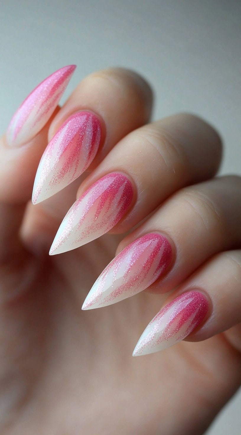 A hand with stiletto nails featuring pink glitter ombré tips streaked with thin, flame-like white details.