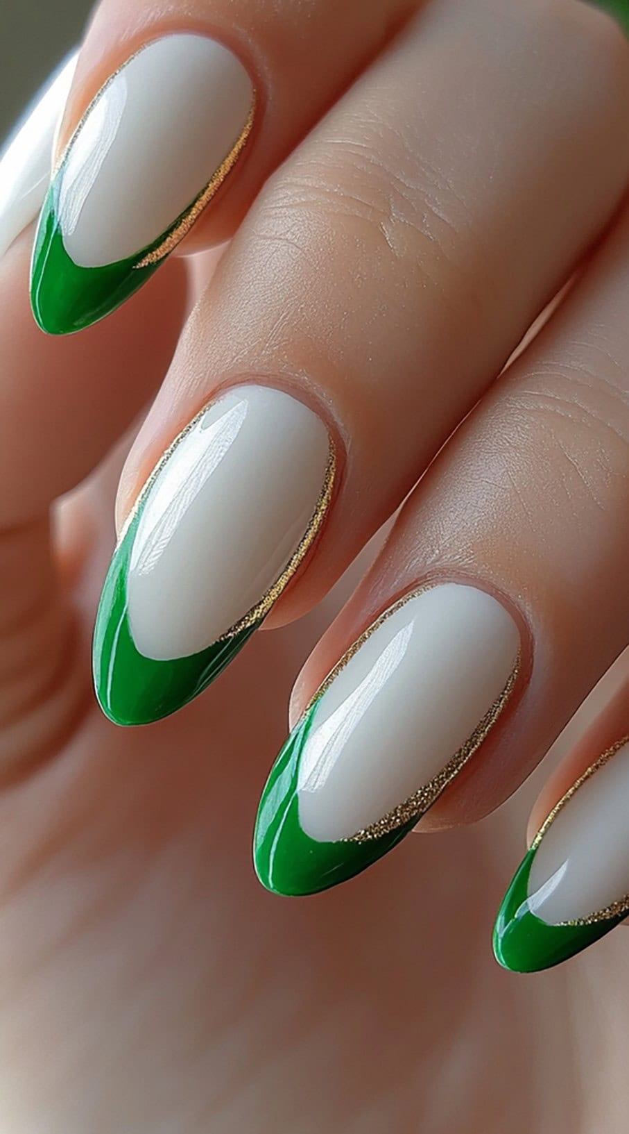 White almond-shaped nails with deep green French tips and fine gold lining.