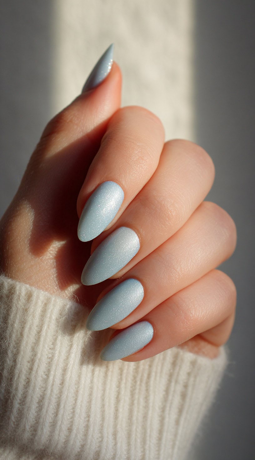 Almond-shaped nails painted in a soft frosty blue with a fine shimmer finish.