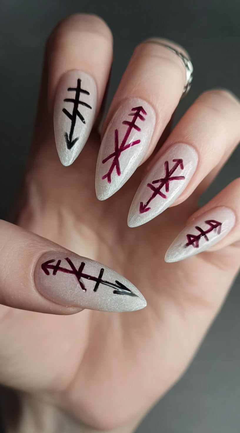 A hand with frosted pearl almond nails featuring sharp burgundy and black bind runes arranged vertically.