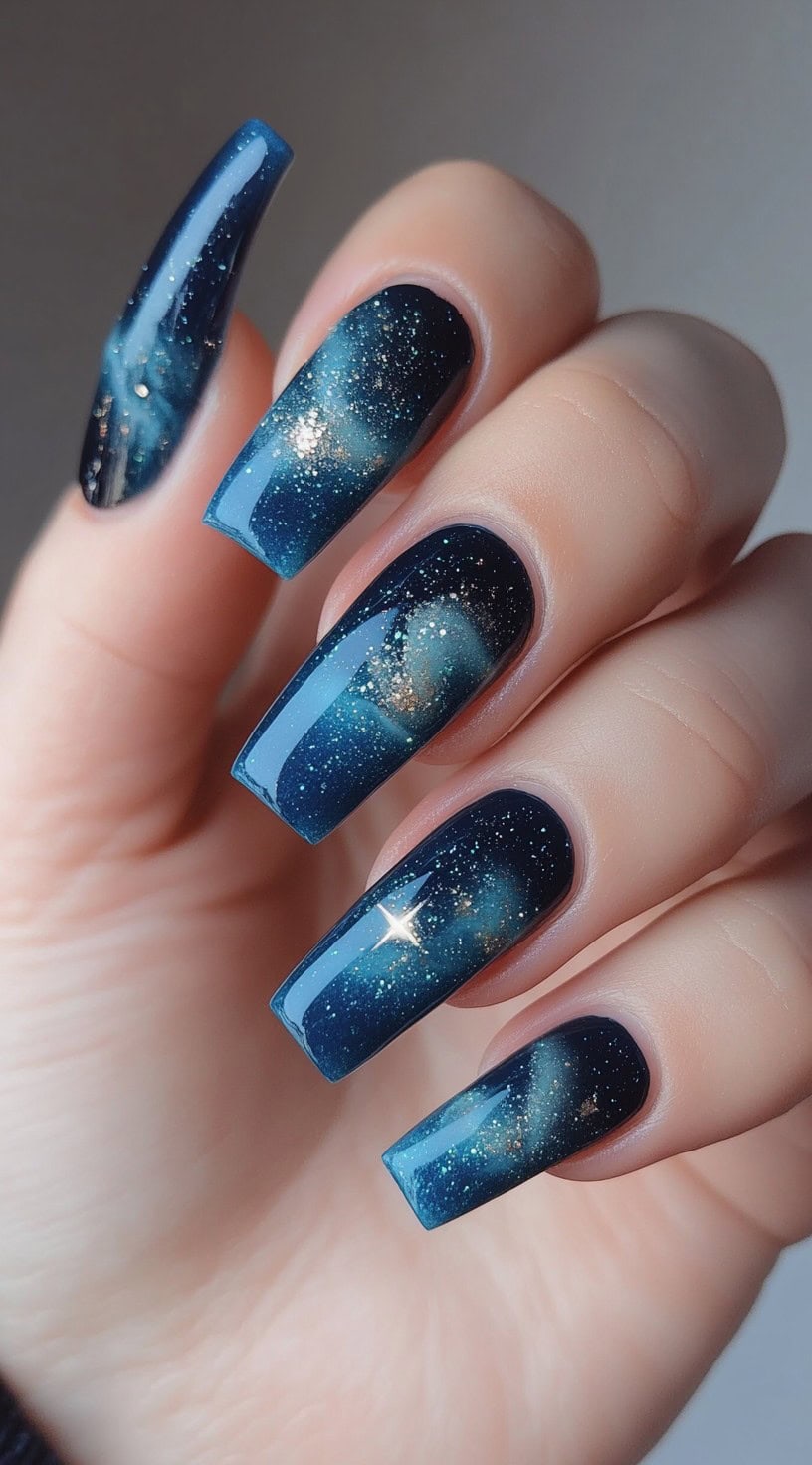 Coffin-shaped nails with a galaxy-inspired ombre in deep blue and teal with golden flecks.