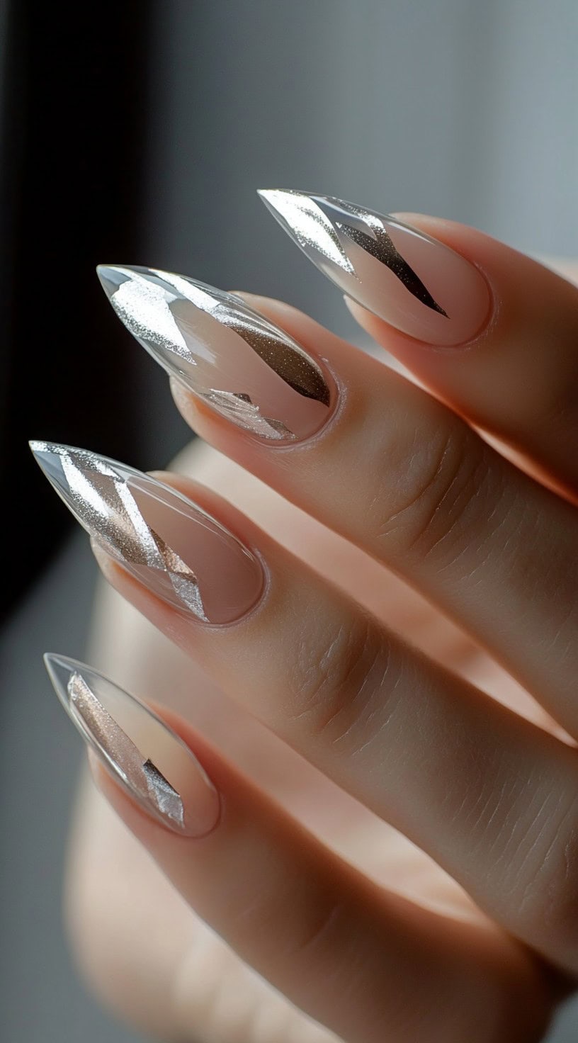 Sharp stiletto-shaped nails with a mix of nude and metallic silver geometric cutouts, creating a bold and modern look.