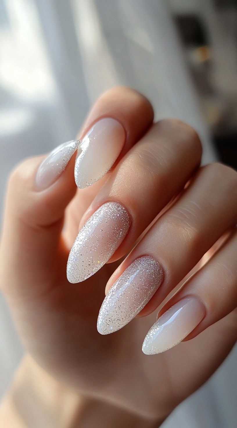 Five almond-shaped nails with an ombré gradient from sheer white to dense silver glitter at the tips.