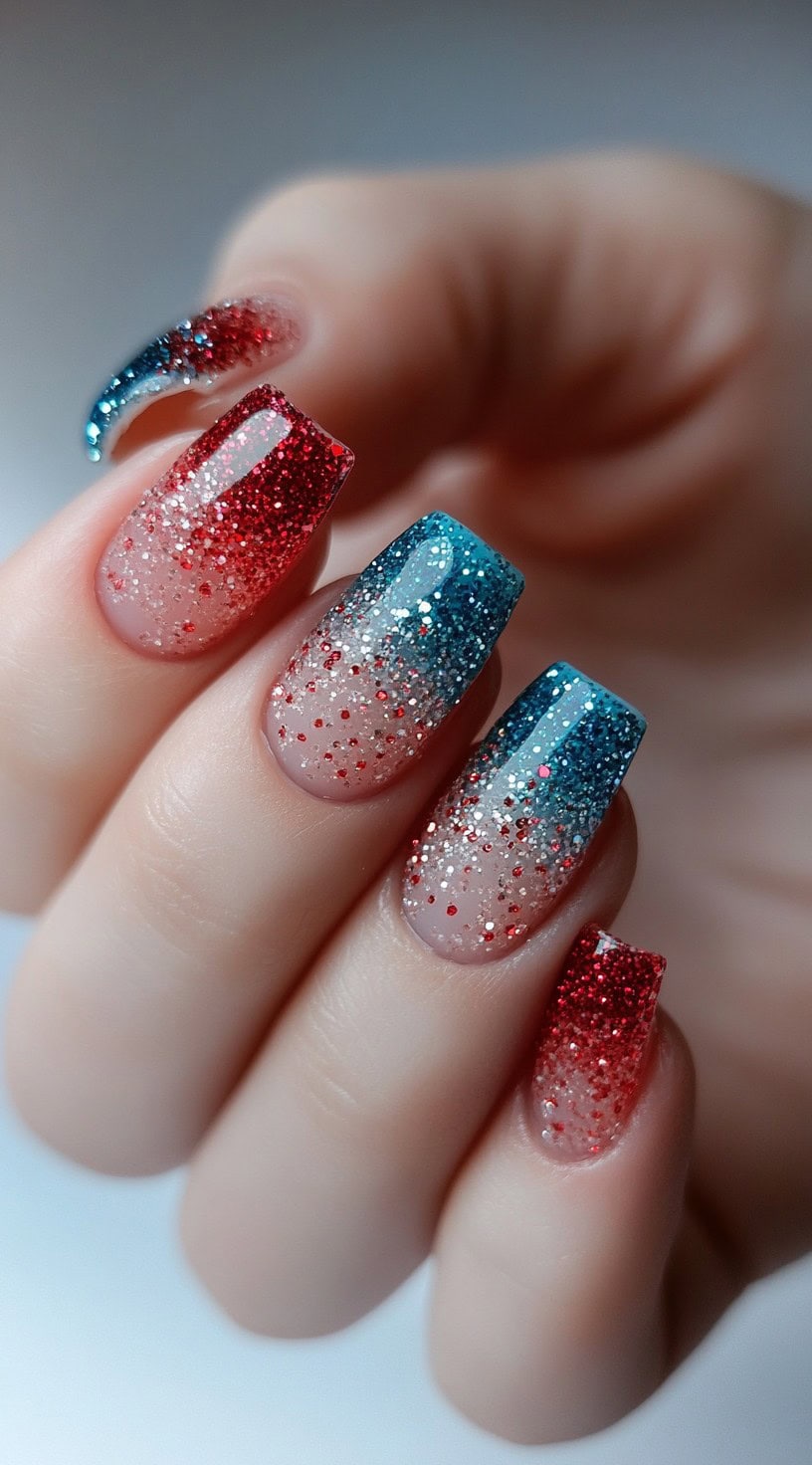 A hand with long nails featuring a glitter ombre effect transitioning from red to blue, creating a dazzling sparkle.
