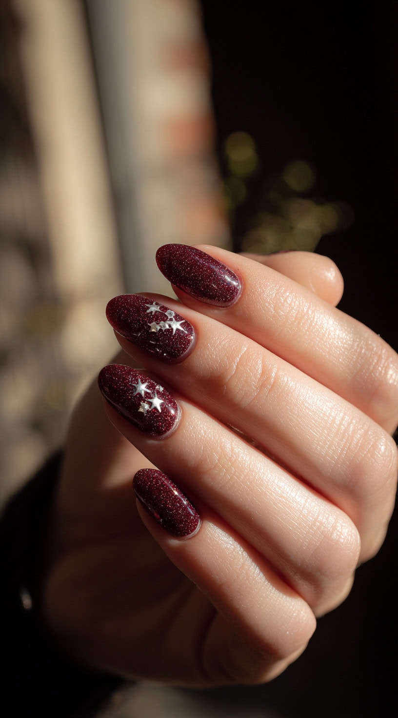 A hand with sparkly wine red nails topped with tiny silver star decals, glistening in the light.