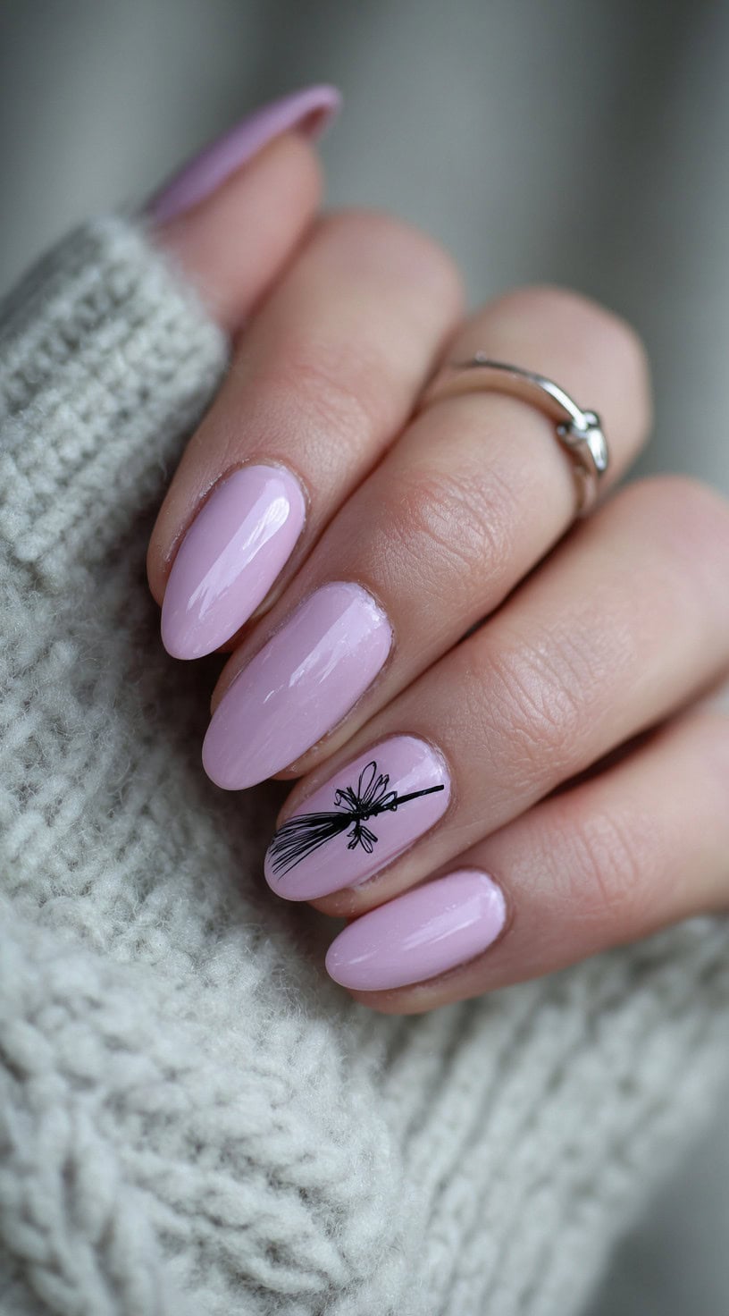 Almond-shaped nails painted pastel pink with a black broomstick illustration on the ring finger.