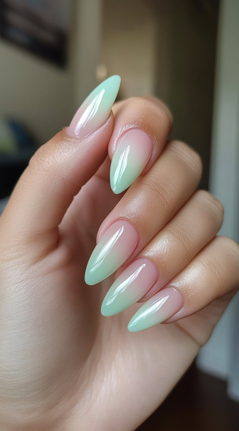 A hand with glossy almond-shaped nails featuring a pink to mint green ombre effect.