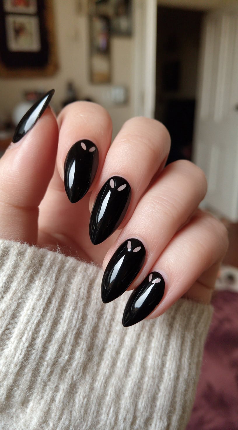 Almond-shaped nails painted entirely in glossy black, with each nail featuring a small pair of pale cat eyes near the cuticle.
