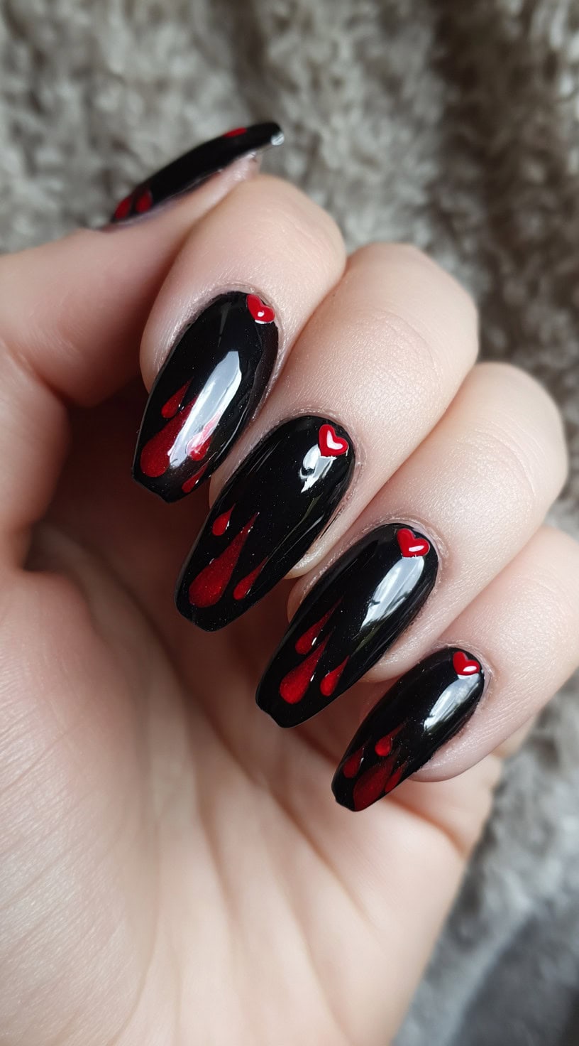 Glossy black coffin nails with red flame-like drips and small red heart details near the cuticle.