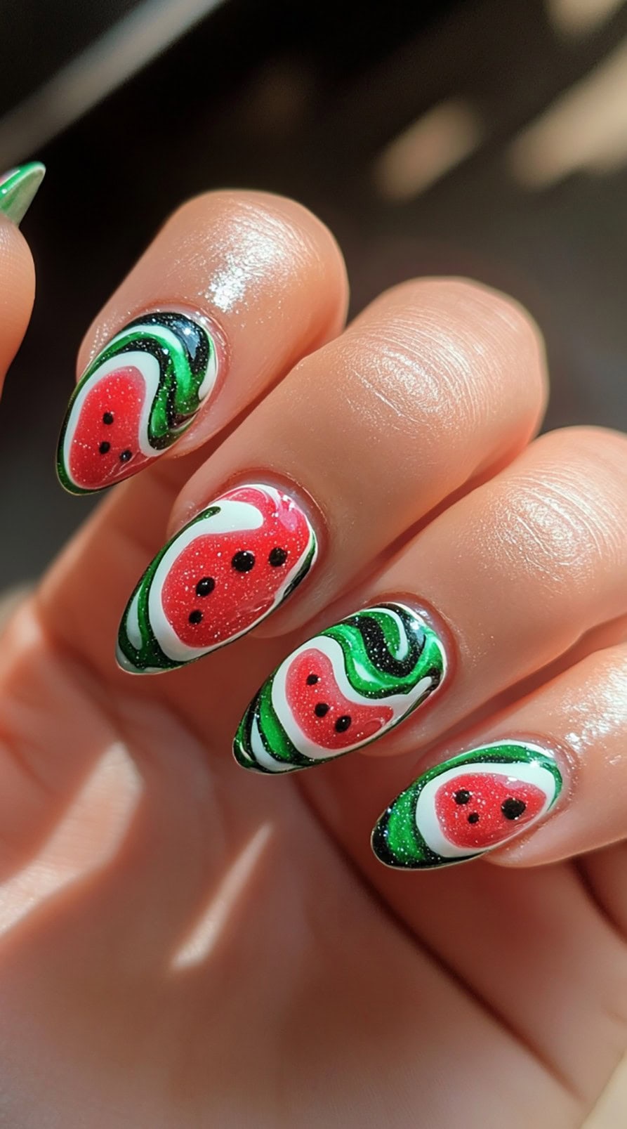Almond-shaped nails featuring glittery watermelon slices framed with bold swirls of green, white, and black.