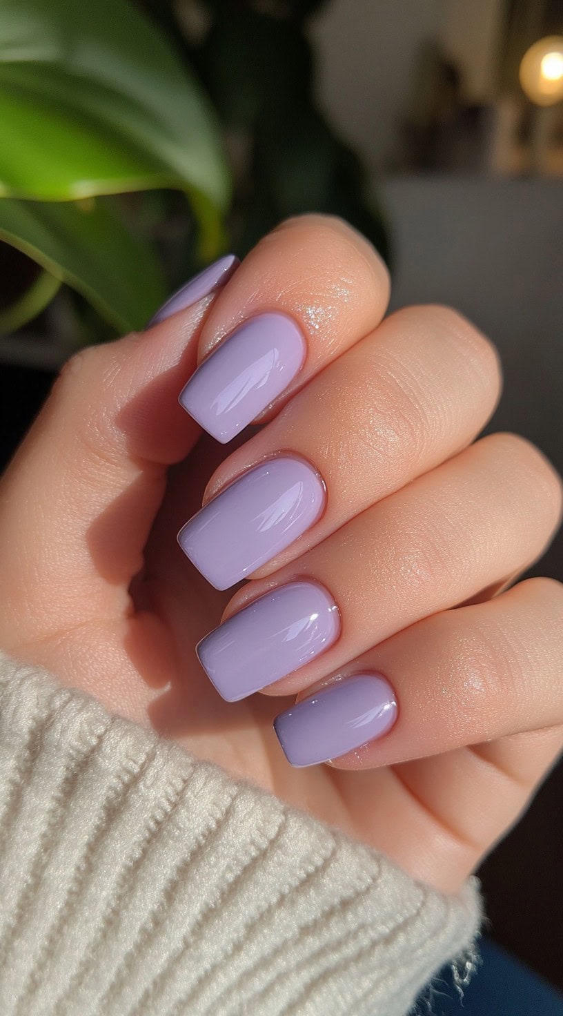 Square-shaped nails painted in a creamy, glossy lilac purple polish under natural light.