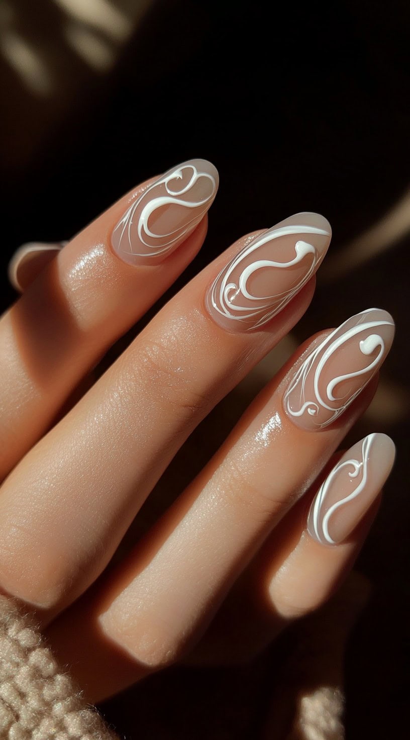 A close-up of a hand with glossy, nude-colored nails featuring abstract white swirl designs for a modern and stylish look.