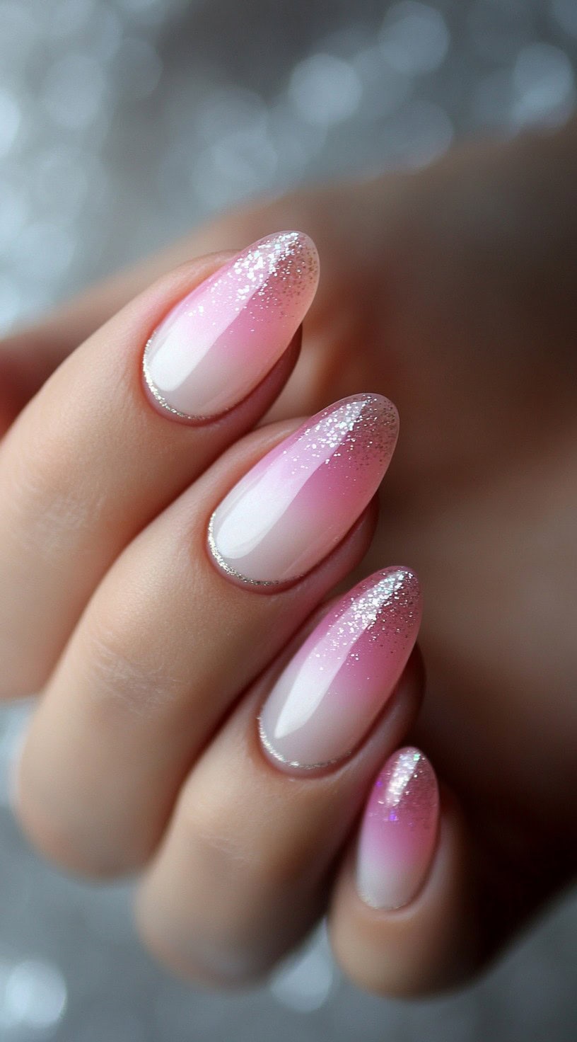 Glossy almond nails with a baby pink to white ombre and a fine silver glitter dusting near the tips.