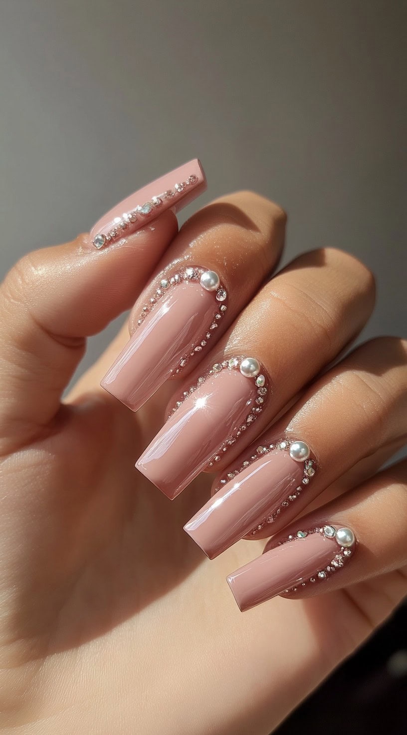 Five glossy pink coffin-shaped nails, each framed with miniature crystals and topped with pearl accents near the cuticle.