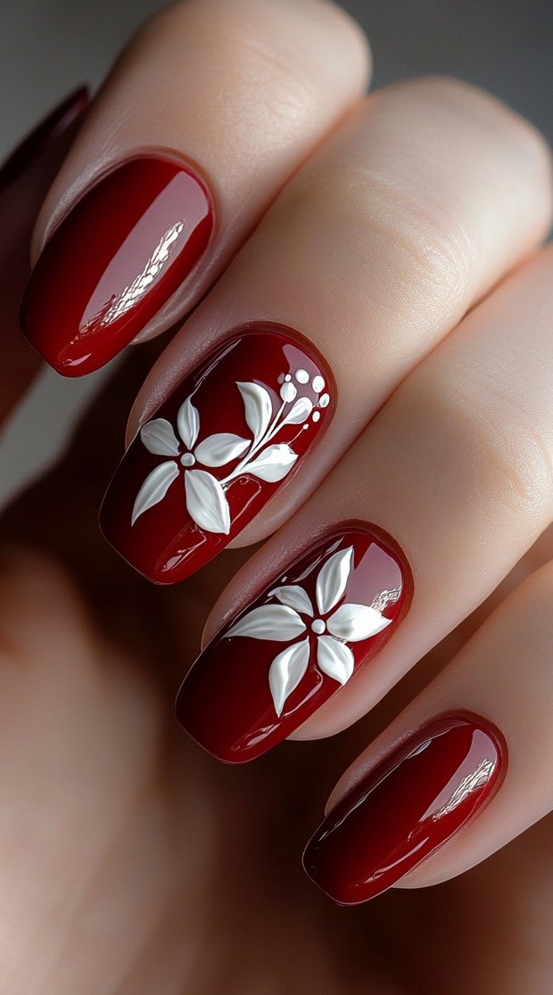 A set of glossy red nails with hand-sculpted white 3D floral designs, giving a soft and romantic bridal aesthetic.