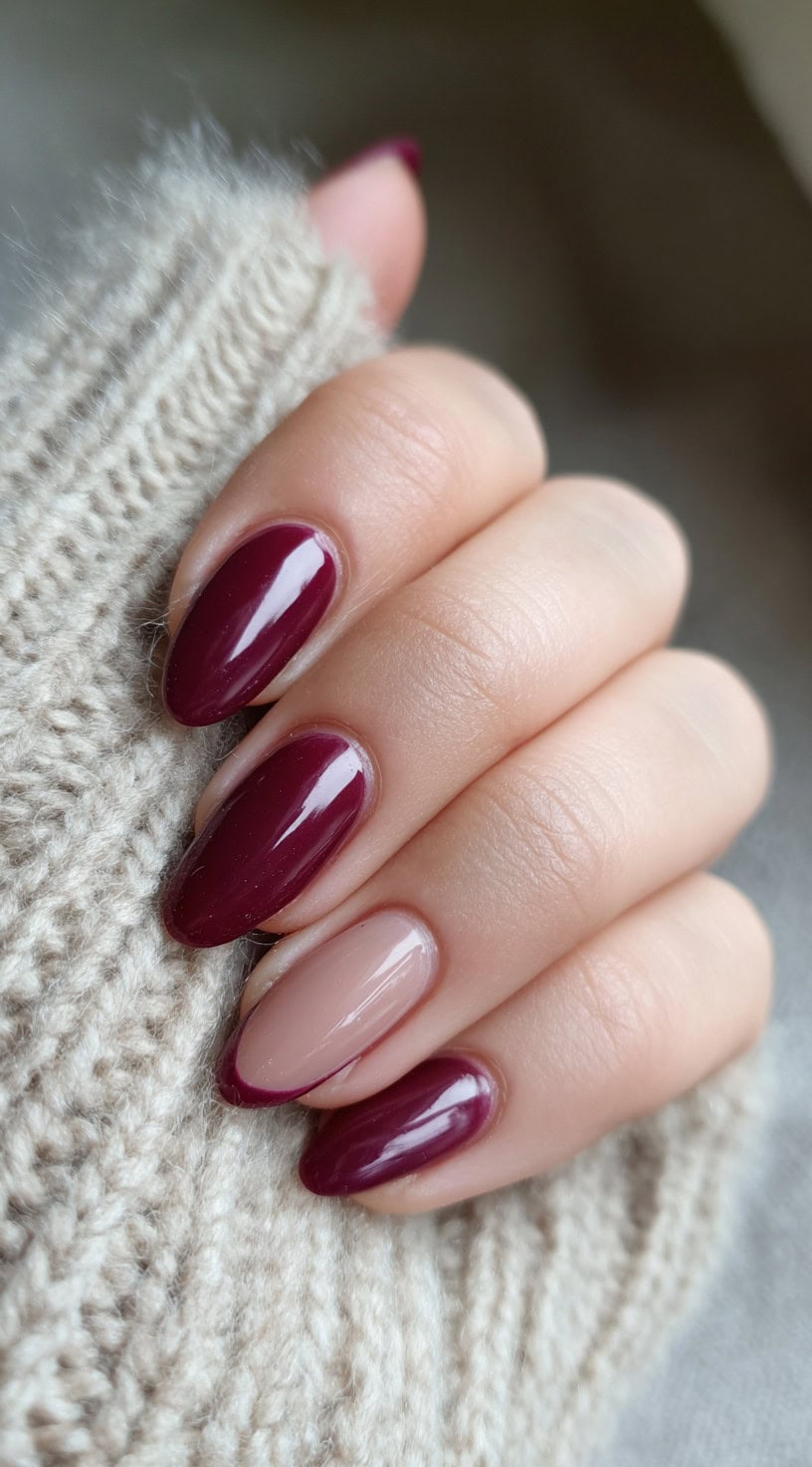 Almond-shaped nails with a glossy wine color and one nude accent nail featuring a deep burgundy French tip.