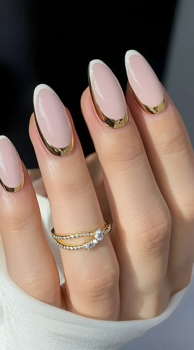 Elegant almond-shaped nails with a nude pink base and metallic gold French tips.