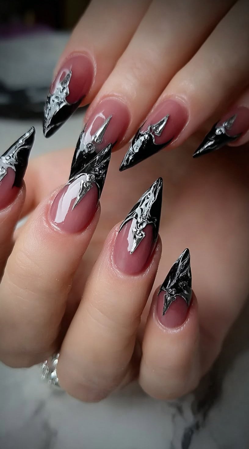 Stiletto nails with glossy nude bases topped by textured black and silver gothic metallic tips.