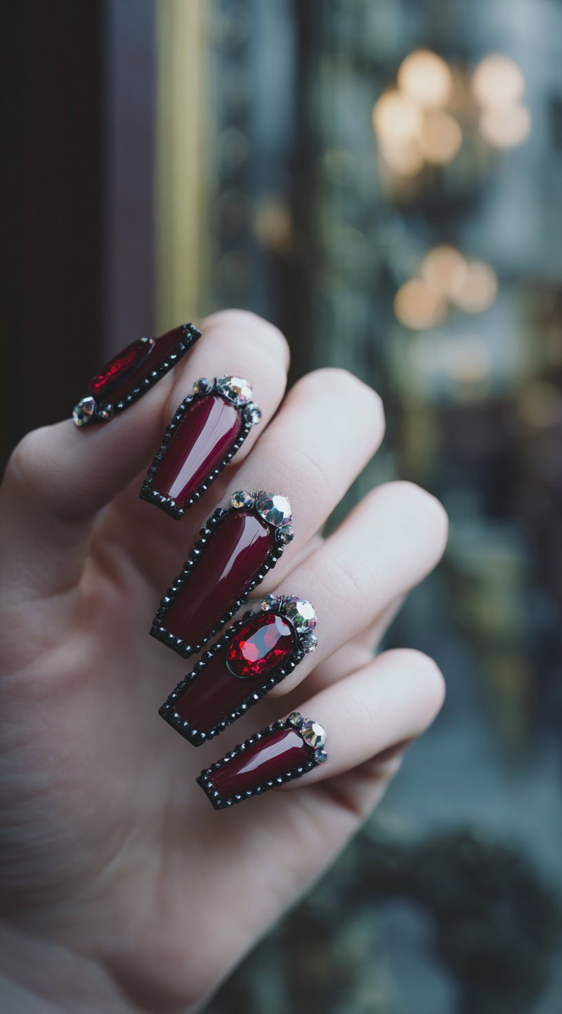 Medium-length coffin nails painted deep burgundy and adorned with large red rhinestones and black bead borders.