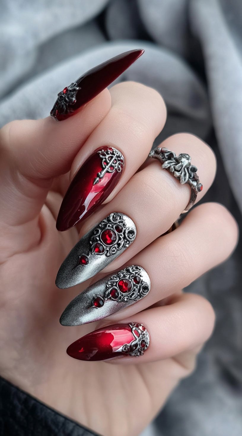Almond-shaped nails combining deep red gloss with metallic silver and intricate ruby-studded embellishments.